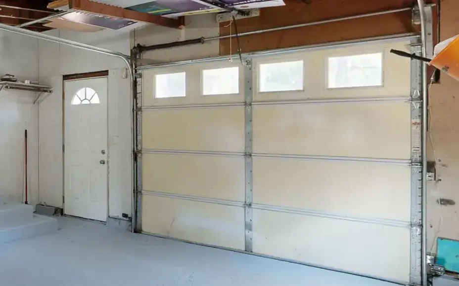 The inside of a closed sectional garage door: the torsion shaft running across the header and the track down the jamb.