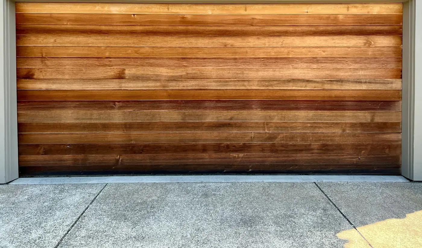 A closed cedar-panelled sectional garage door in its painted surround, seen straight on from the concrete apron.