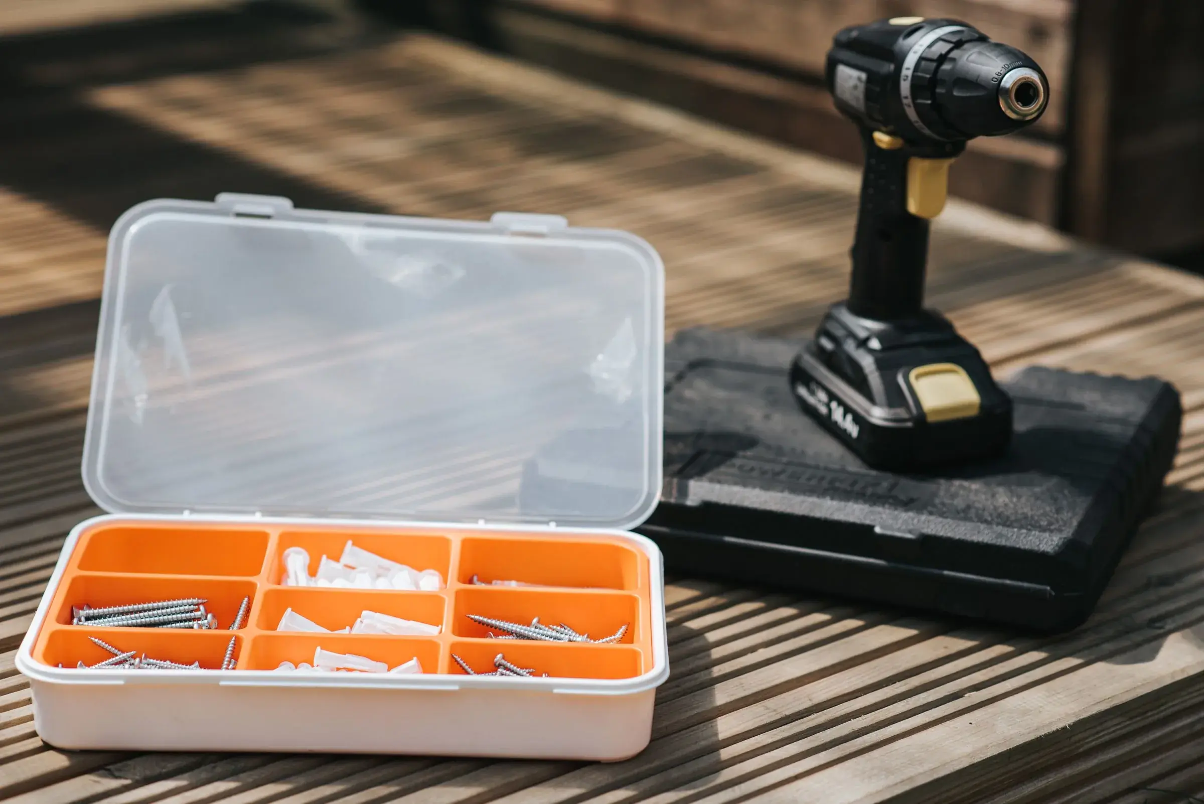 A cordless drill resting on its case beside an open organiser of screws and wall anchors.